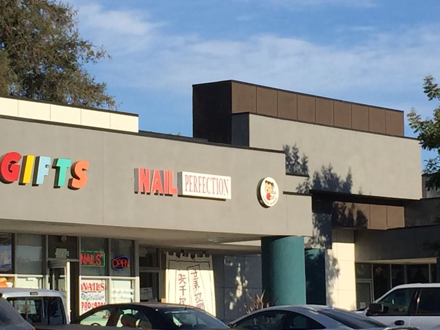Nails Perfection in the Warm Springs plaza, coral NAIL PERFECTION letters next to a gift shop and Ajisen Noodle.